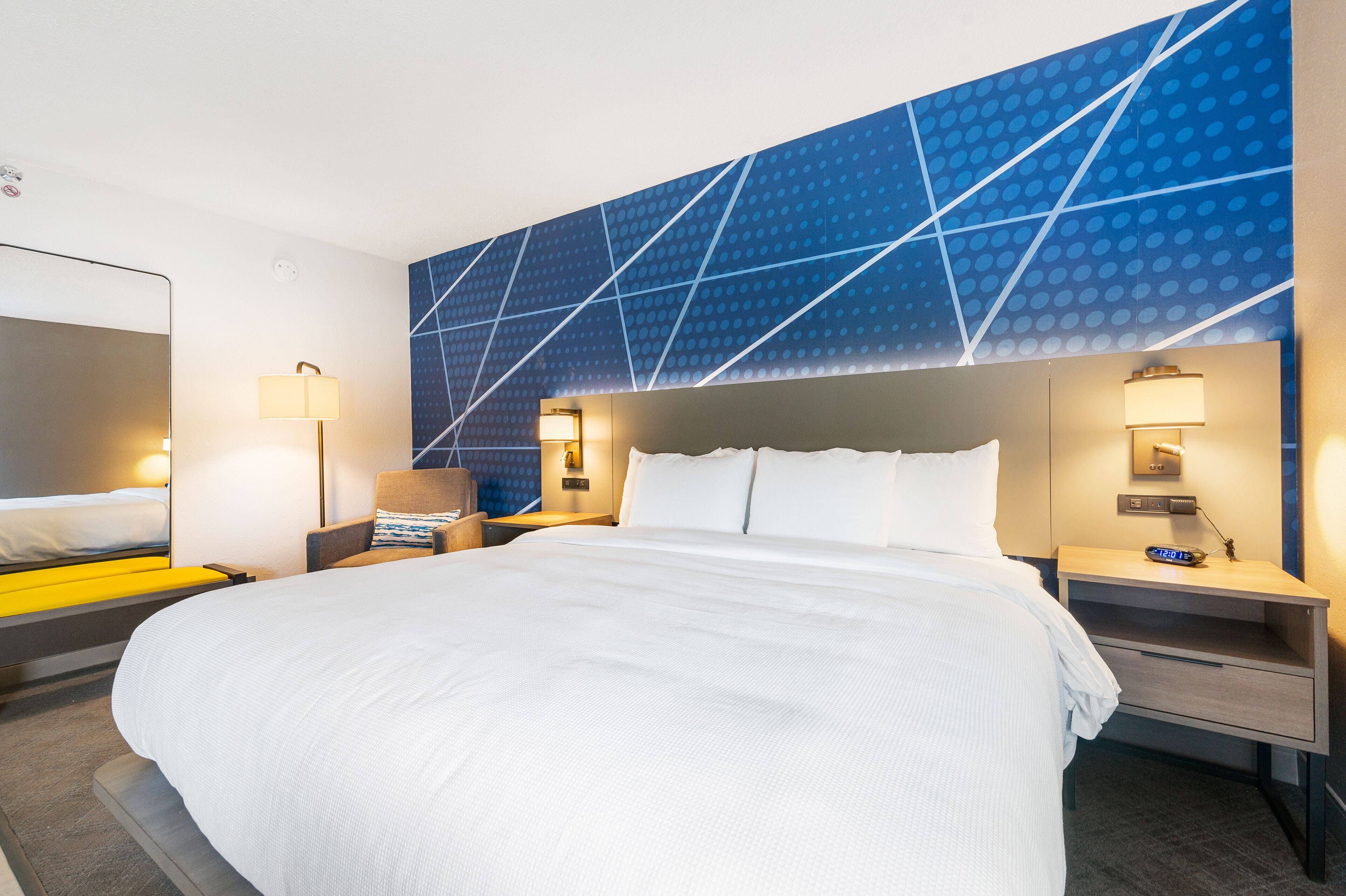 Habitación de hotel con una cama grande, dos mesitas de noche y una pared con diseño geométrico.