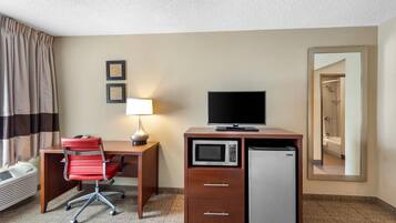 A hotel room with a desk, a chair, a television, a microwave, a mini-fridge, a lamp, and a mirror.
