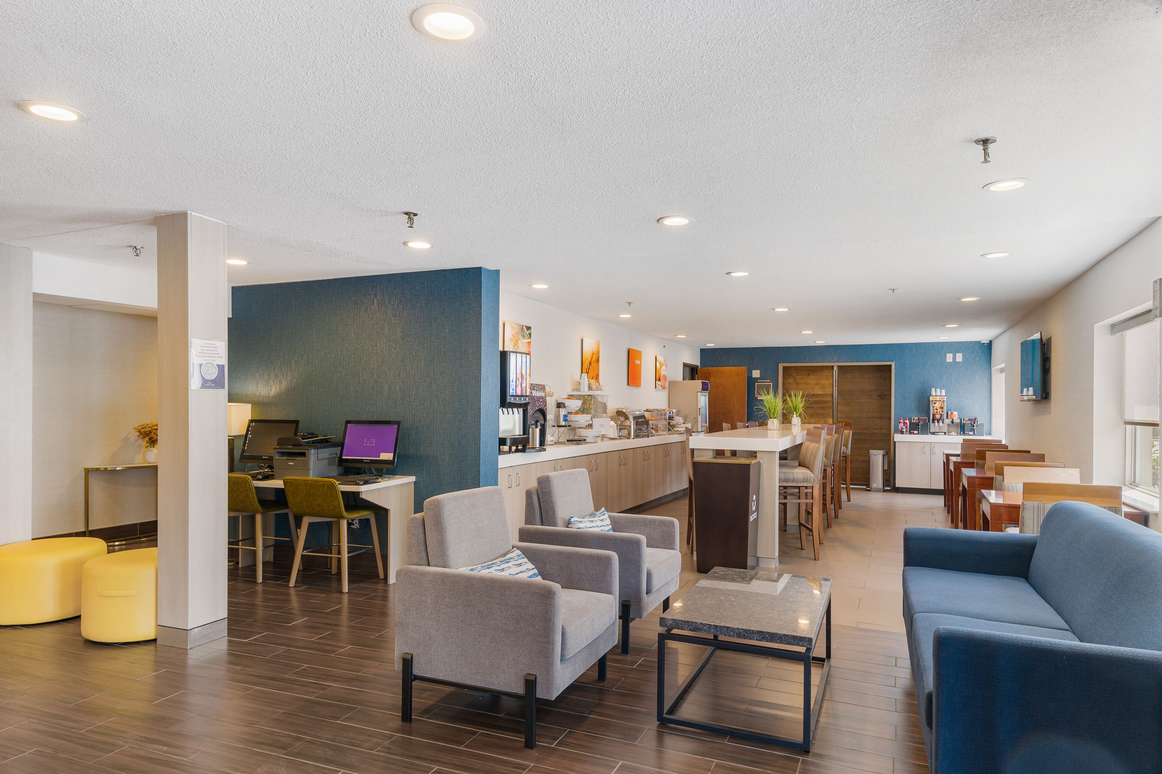 A modern hotel lobby with a reception desk, seating area, and a kitchenette.