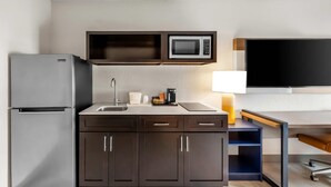 A compact kitchen with a refrigerator, microwave, sink, and a flat-screen TV above the counter.