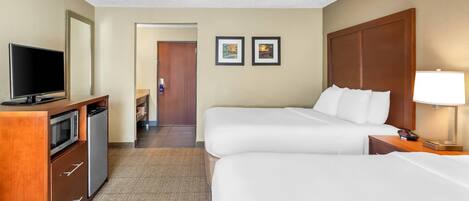 A hotel room with two beds, a TV, a mini-fridge, a desk, and a lamp.