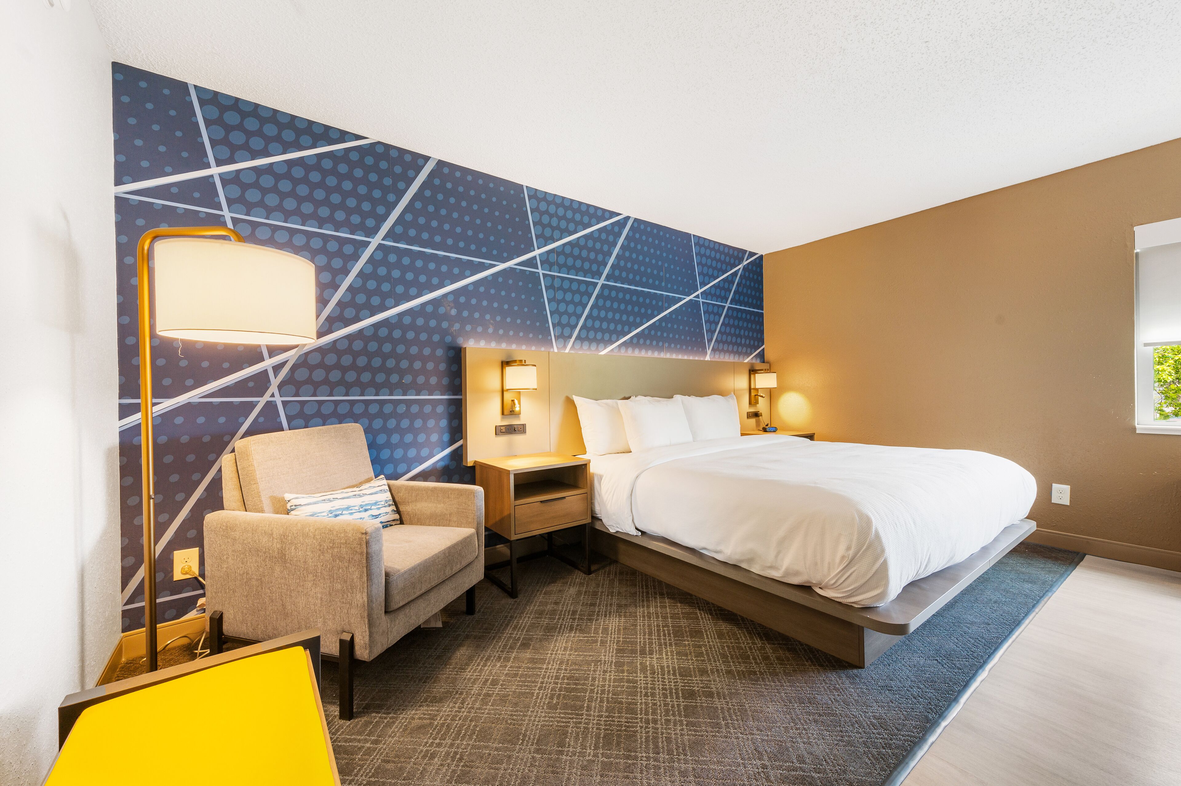 Une chambre d’hôtel avec un lit, une chaise, un bureau et un mur orné d’un motif géométrique.