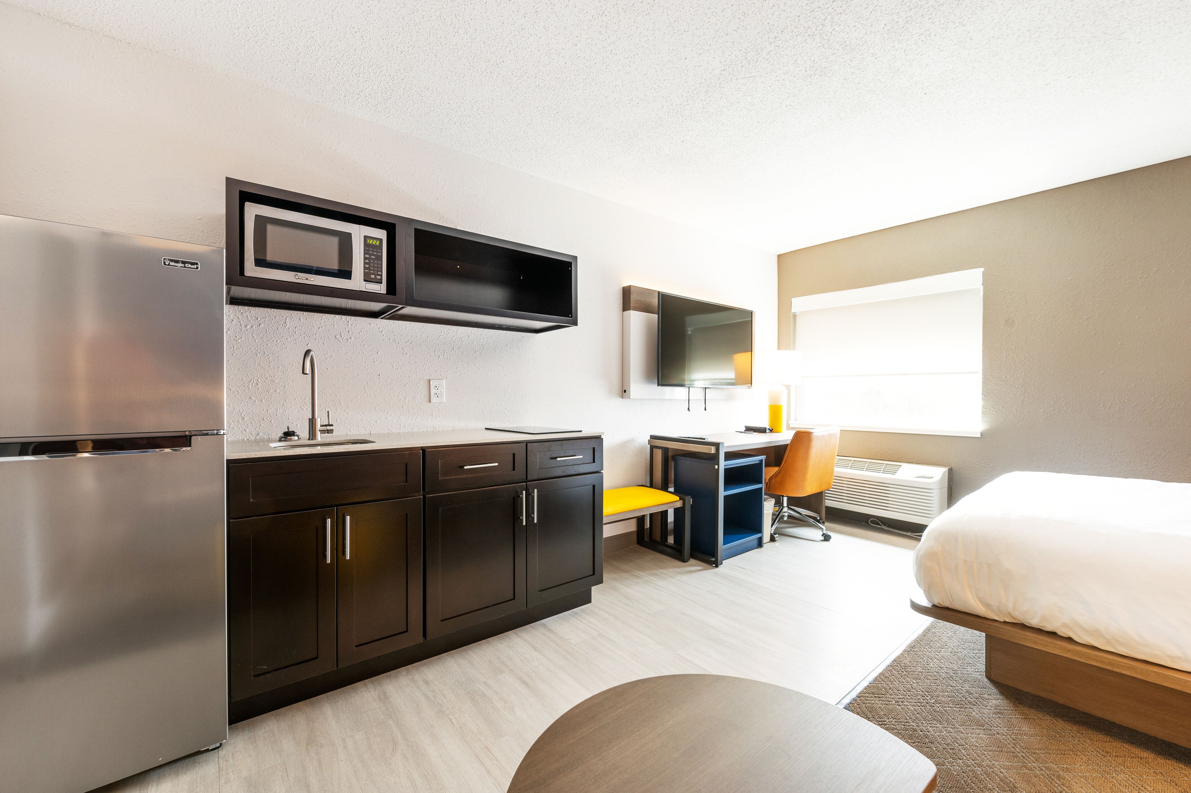 Una habitación de hotel moderna con kitchenette, cama, televisión y ventana.
