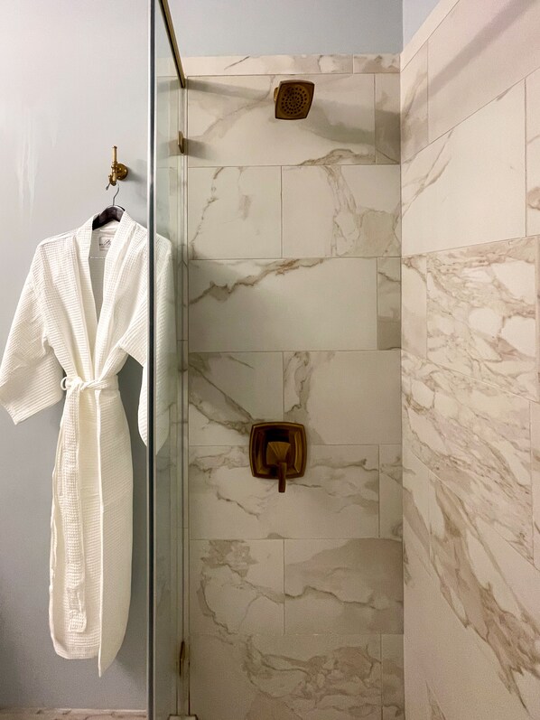 Une salle de bain dotée d’une douche à parois de verre, de carreaux de marbre et d’un porte-serviettes sur lequel est posé un peignoir blanc.