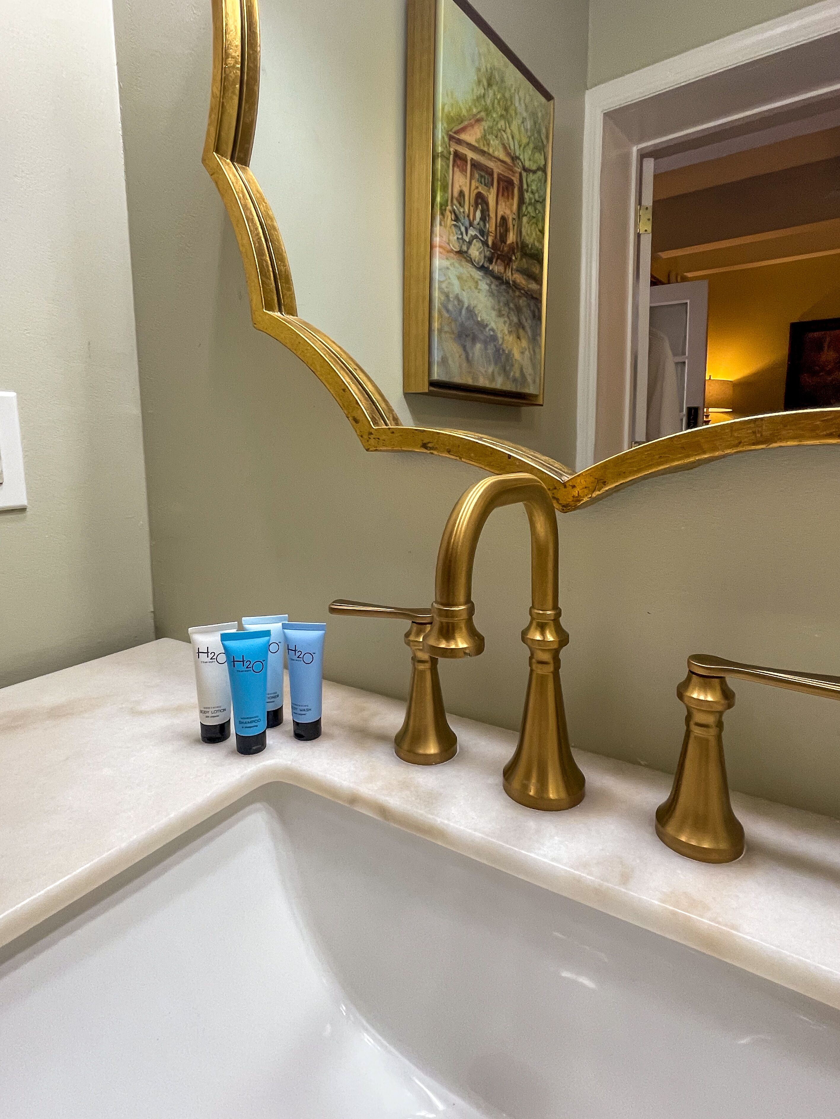 A bathroom with a gold-framed mirror, a sink, and toiletries on the counter.
