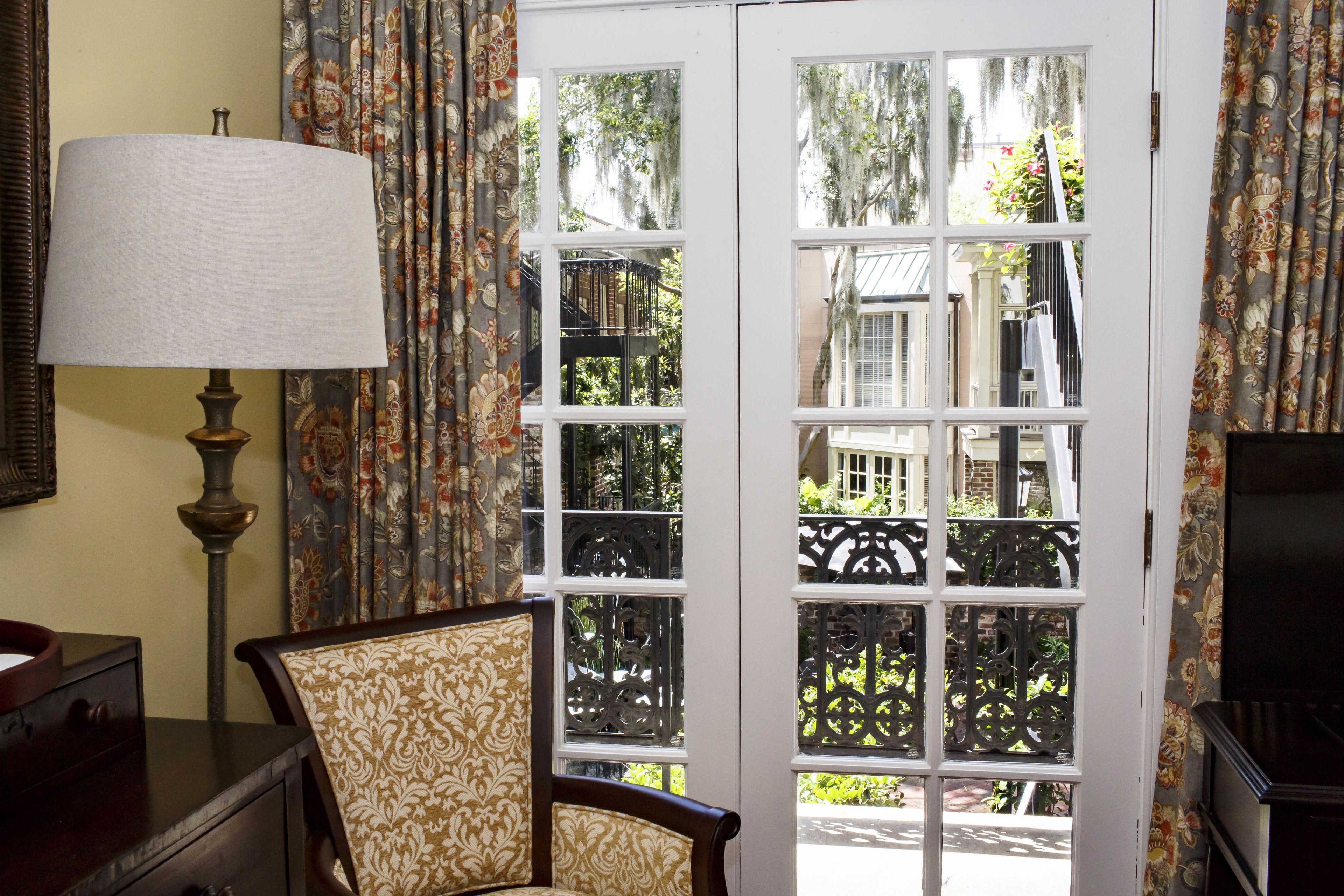 A room with a large window, a lamp, a chair, and a dresser.