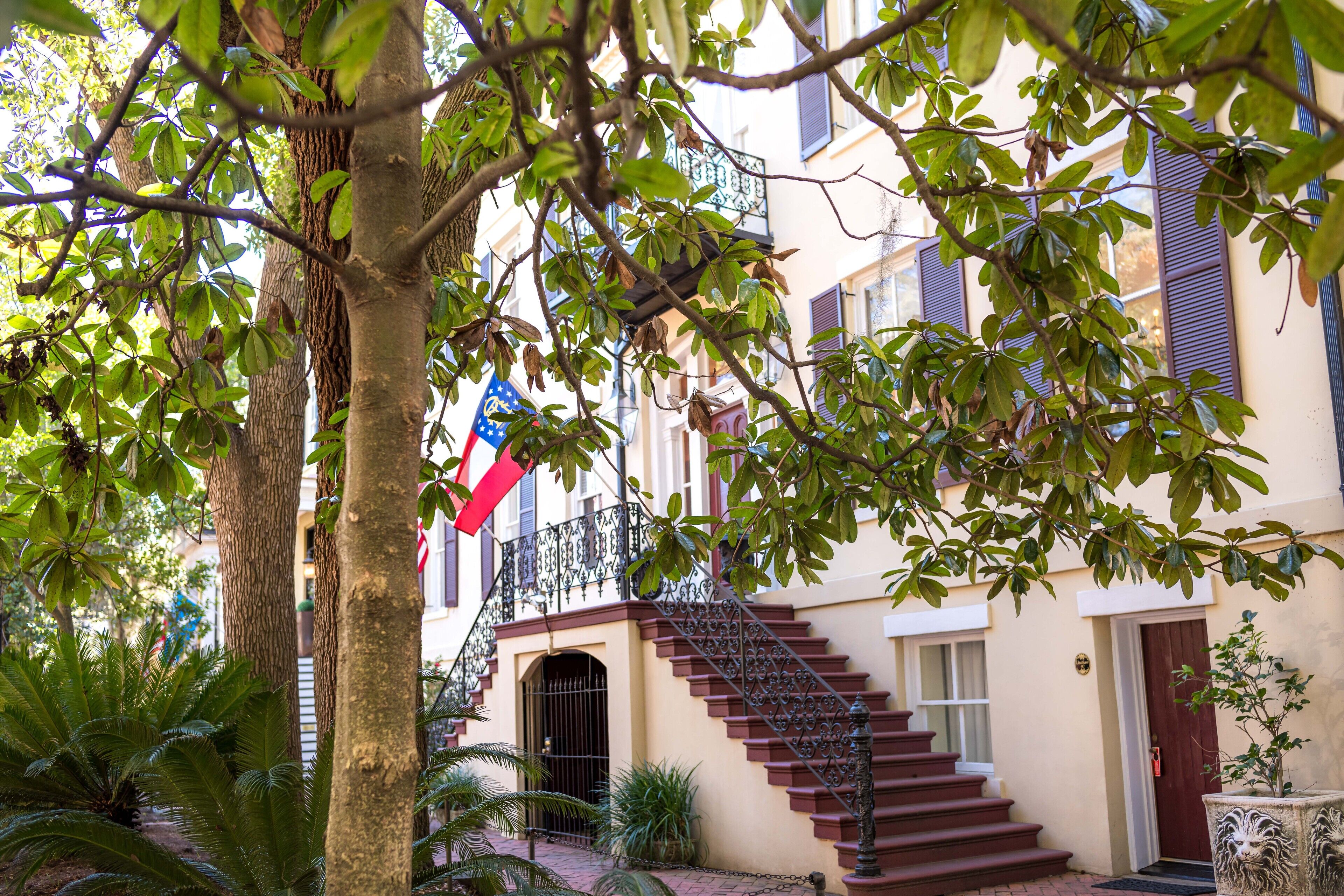 A building with a staircase leading to a door, surrounded by trees and plants.