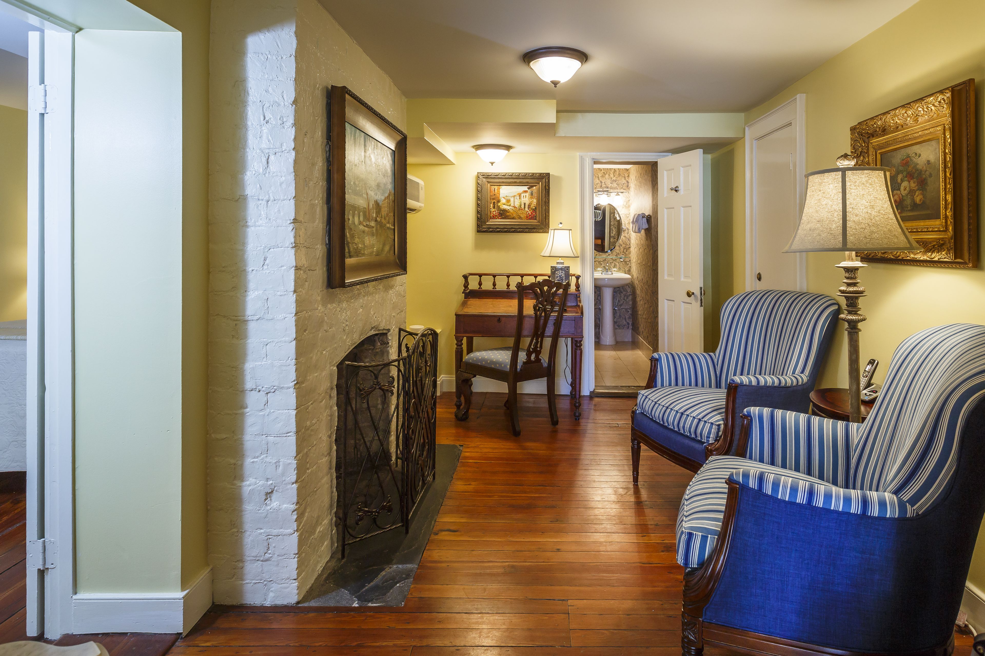 A cozy living room with a fireplace, striped armchairs, a dining table with chairs, and a hallway leading to a bathroom.