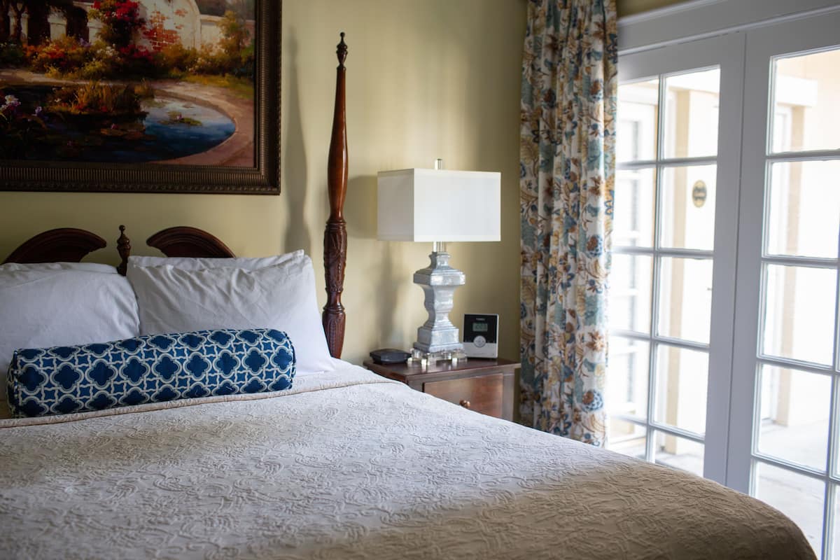 A neatly made bed with a patterned pillow, a bedside table with a lamp, and a painting on the wall.