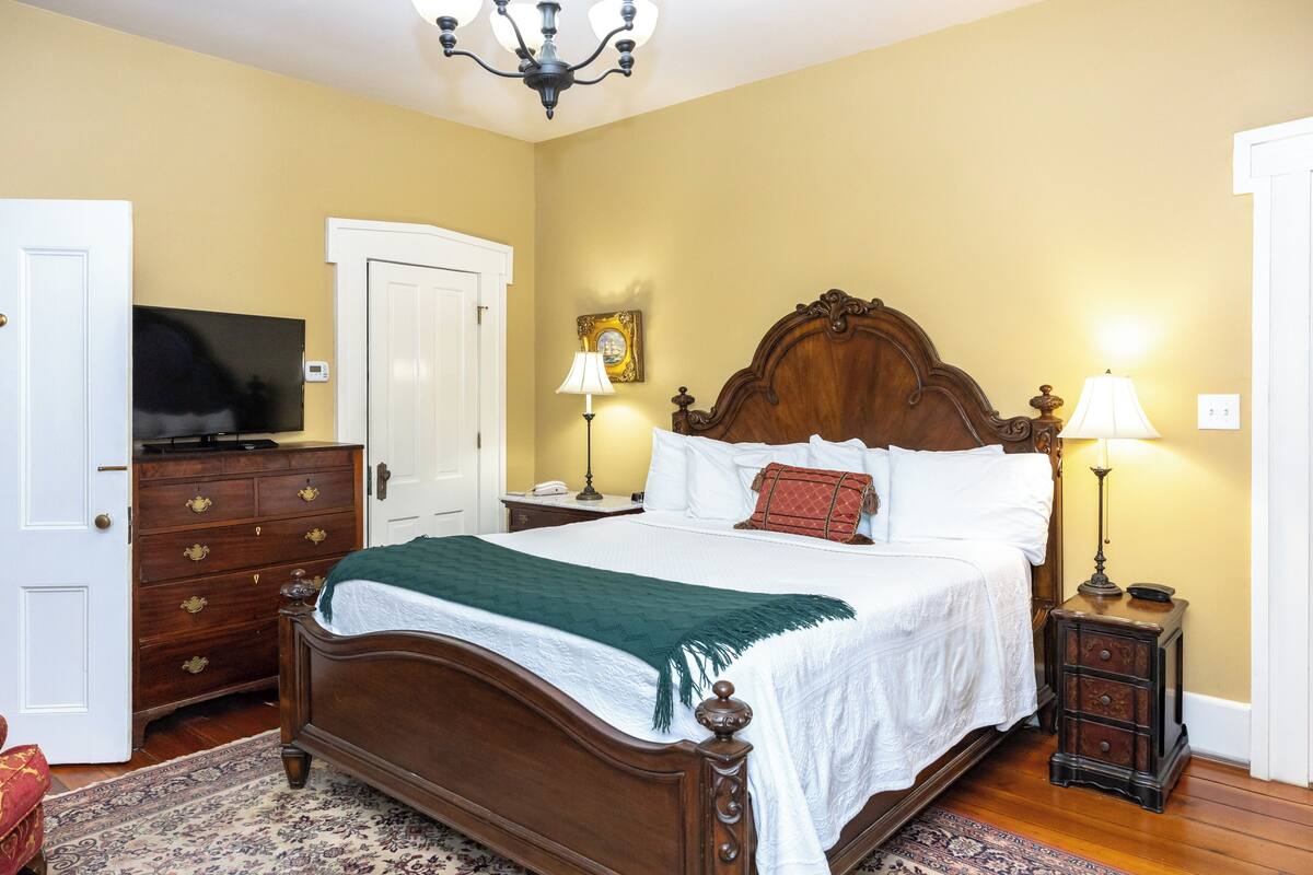 A bedroom with a wooden bed, a television on a dresser, two bedside lamps, and a door.