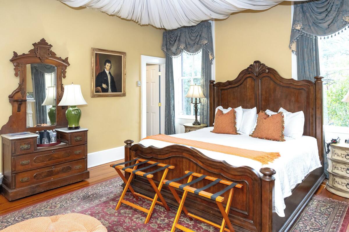 A bedroom with a large bed, wooden dresser, and a mirror.