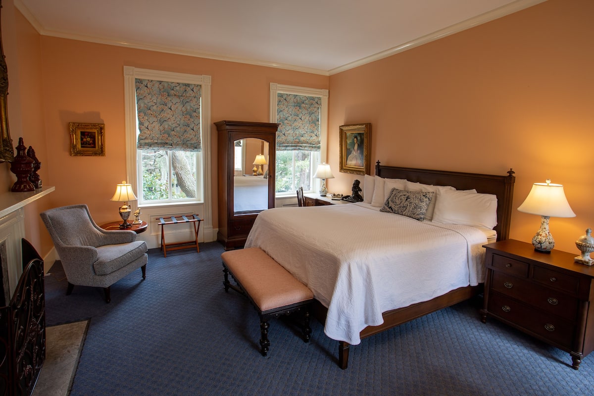 A bedroom with a large bed, a chair, a bench, a nightstand, and a dresser.