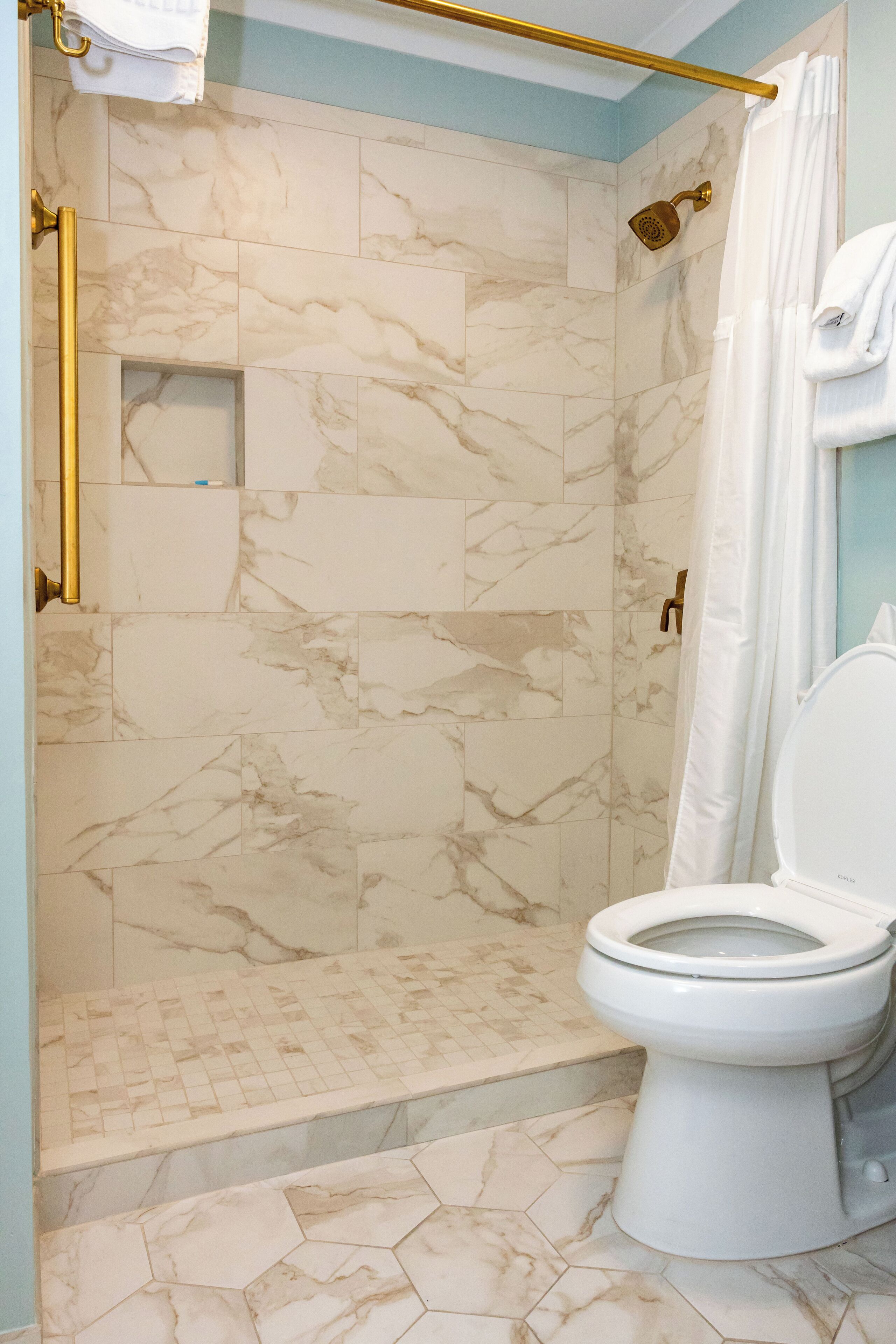 A bathroom with a shower, toilet, and marble tiles.