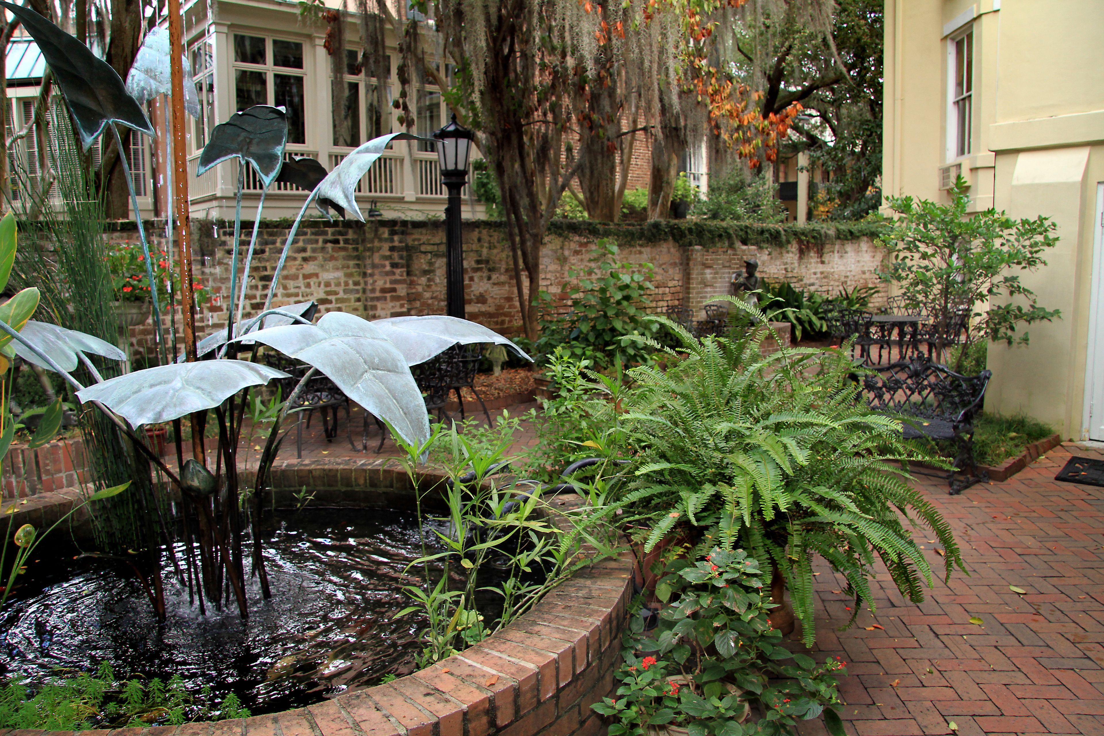 A brick garden with a pond, ferns, and umbrellas.