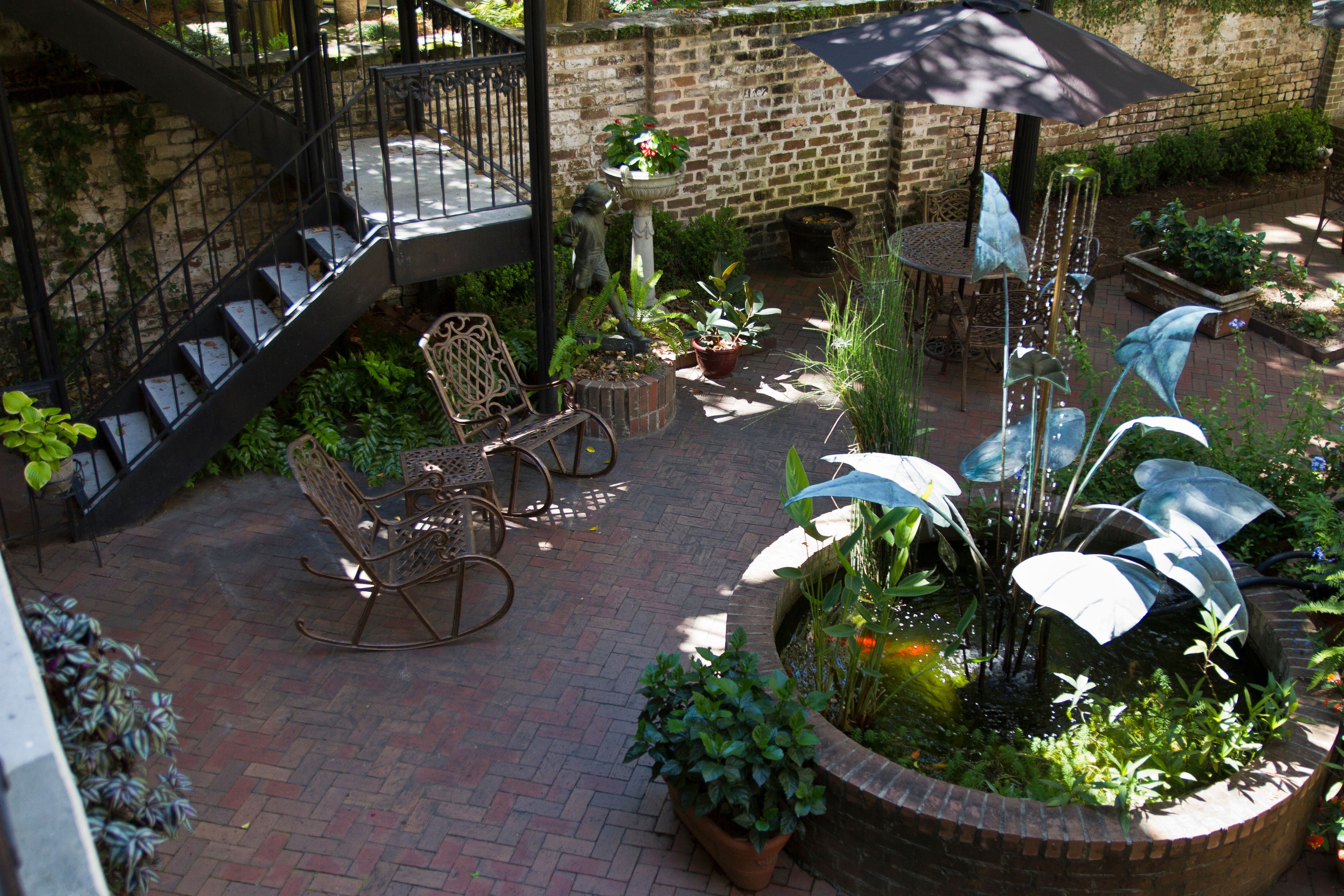 Eine Terrasse mit Ziegelpflaster, einem Brunnen, Kübelpflanzen und Gartenmöbeln.