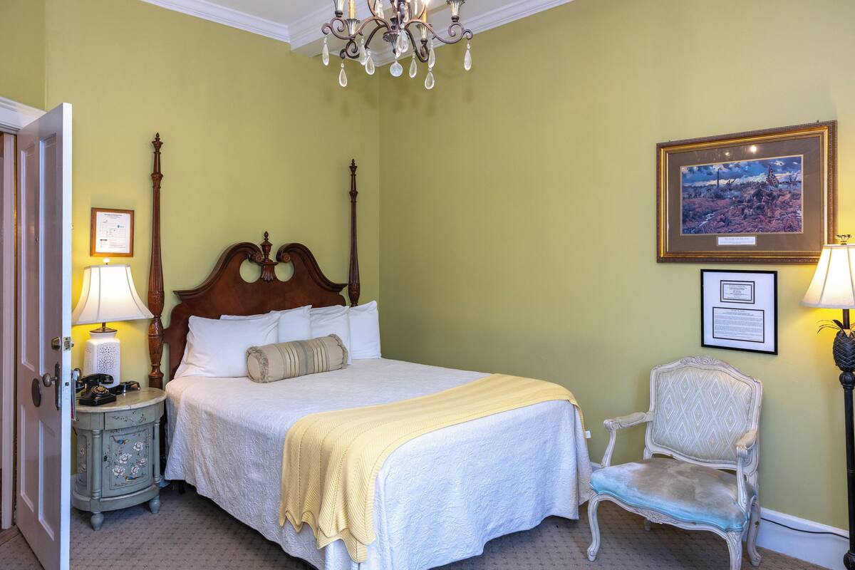 A neatly made bed with a wooden headboard, two bedside lamps, a chair, and framed pictures on the wall.
