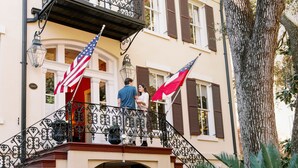 Um edifício com varanda, bandeiras americanas e uma árvore.