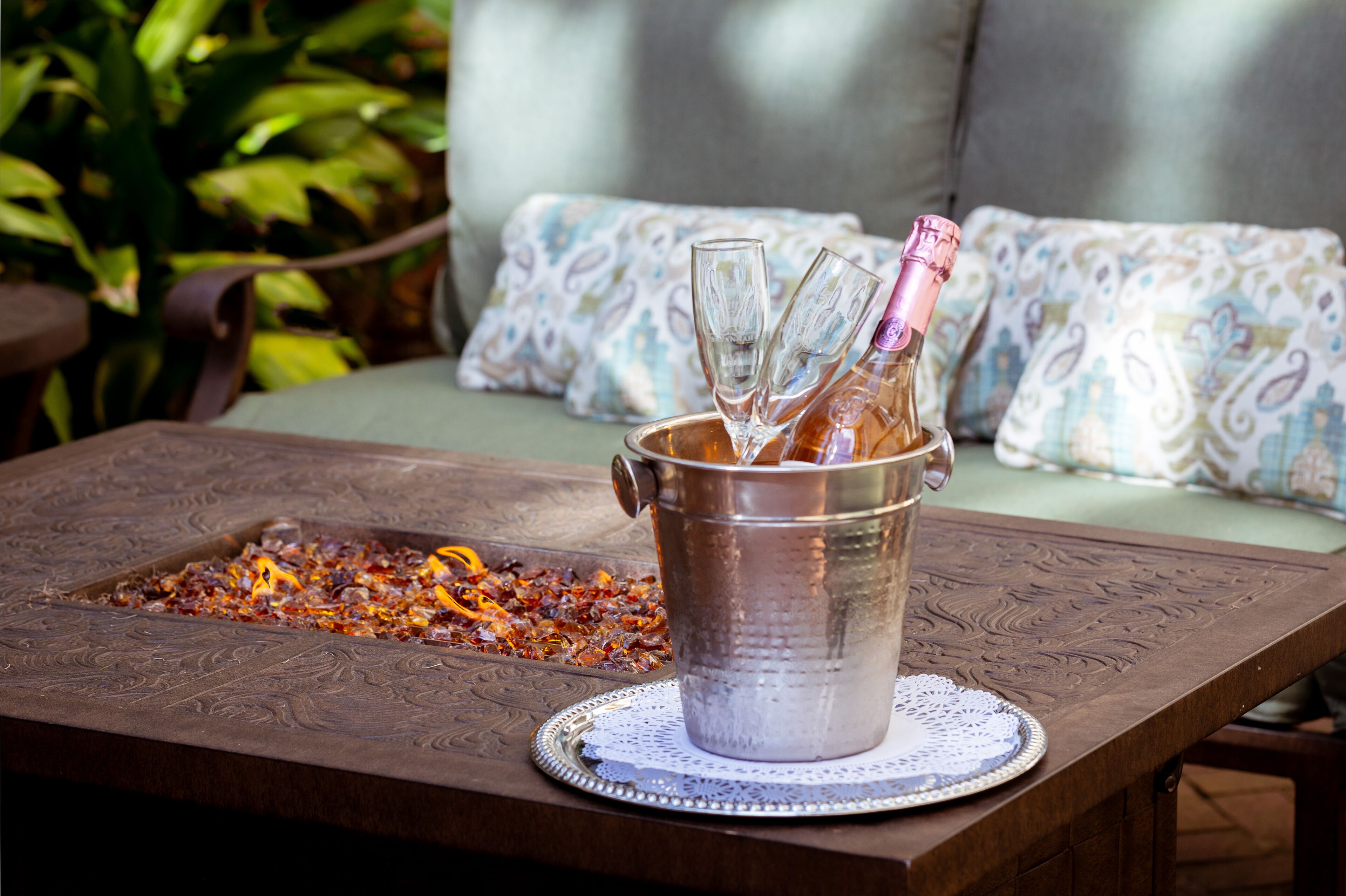 A metal bucket with a bottle and glasses on a table with a decorative doily.