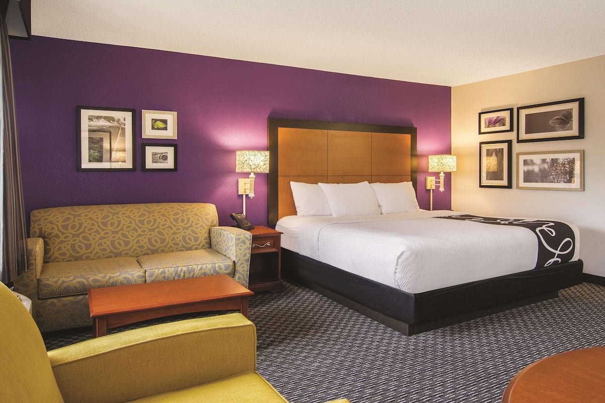 A hotel room with a bed, a sofa, a small table, and a nightstand with lamps.