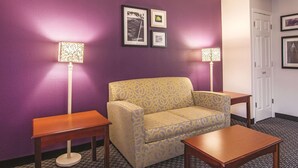 A room with a purple wall, a patterned sofa, two wooden tables, and two floor lamps. - Wingate by Wyndham Brunswick GA / I-95 (Brunswick)