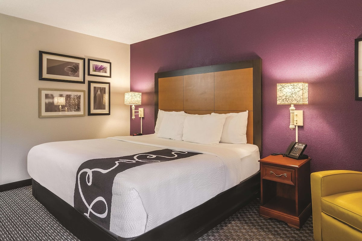 A hotel room with a large bed, two bedside lamps, a wooden nightstand, a telephone, and a chair.