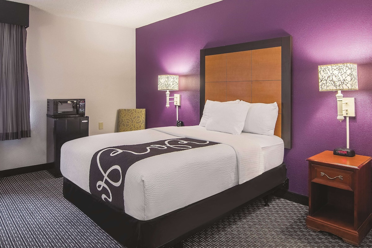 A hotel room with a bed, two bedside lamps, a nightstand, a microwave, and a patterned pillow.