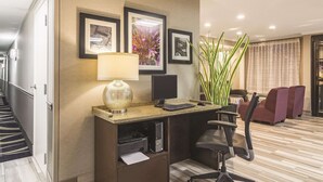 A hotel office with a desk, computer, chair, and a plant. - Wingate by Wyndham Brunswick GA / I-95 (Brunswick)