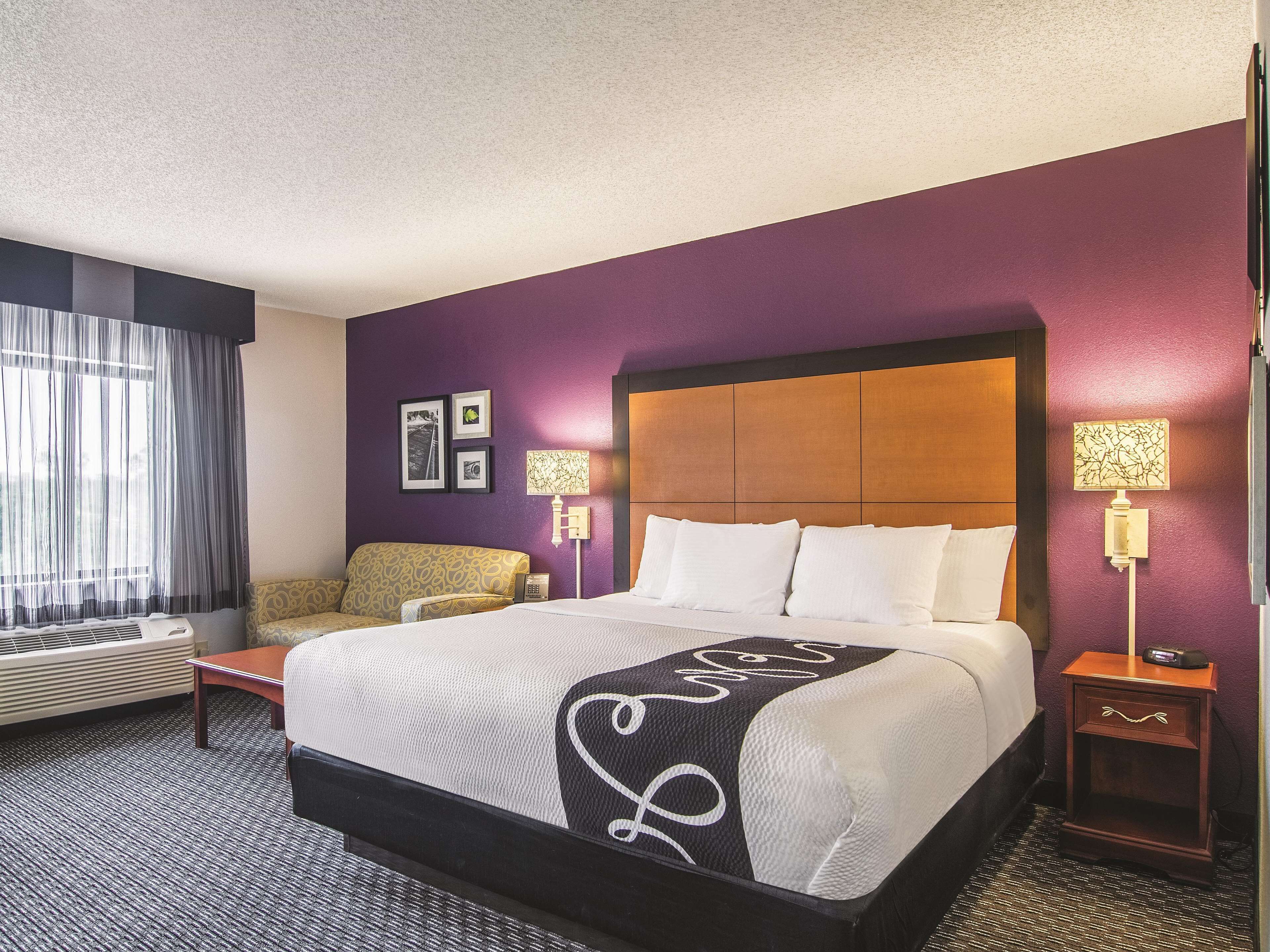 A hotel room with a large bed, a sofa, a bedside table, and a lamp.
