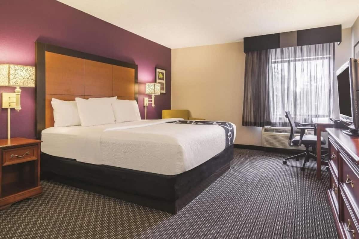 A hotel room with a large bed, a desk, a chair, a television, and a window with curtains.