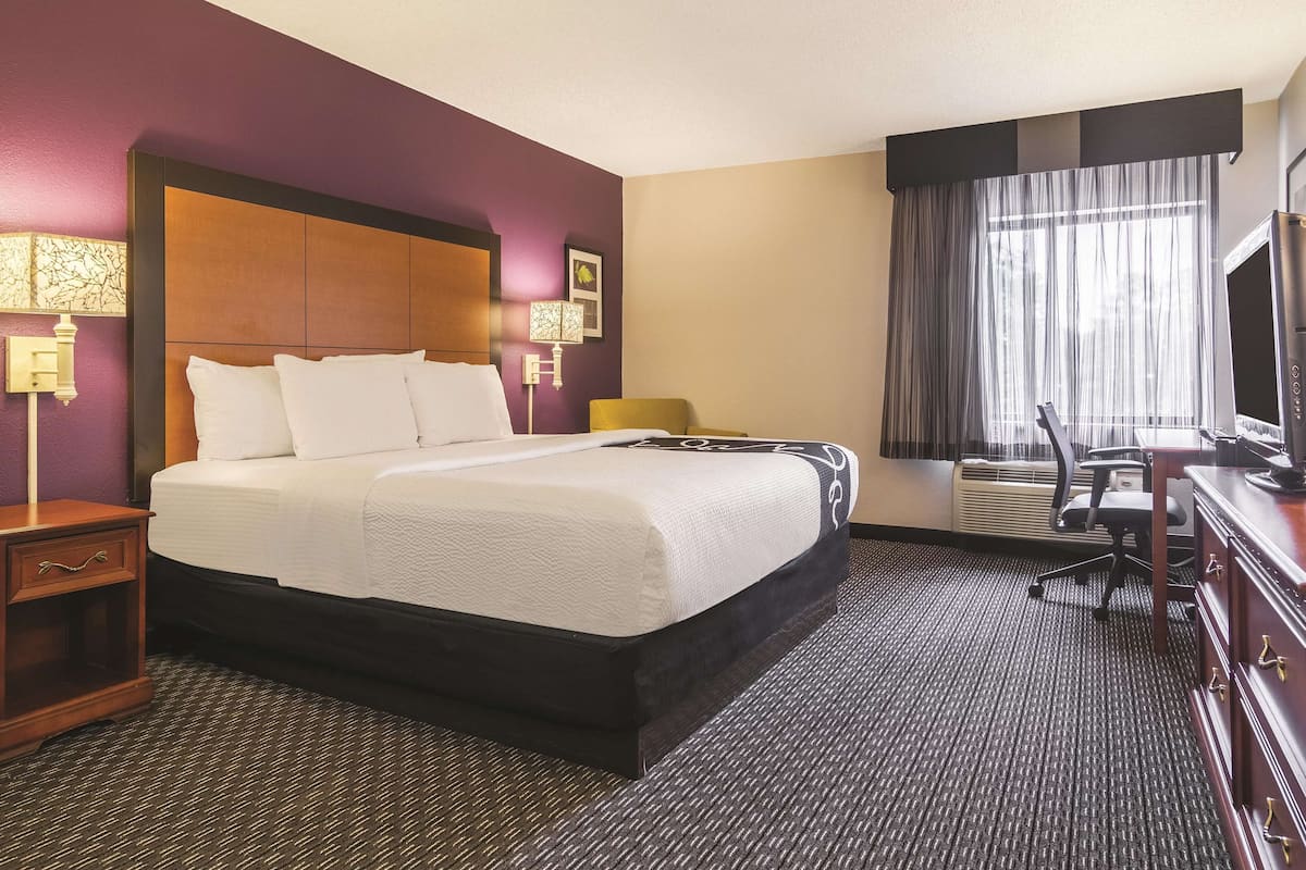A hotel room with a large bed, a desk with a computer, a chair, and a TV.