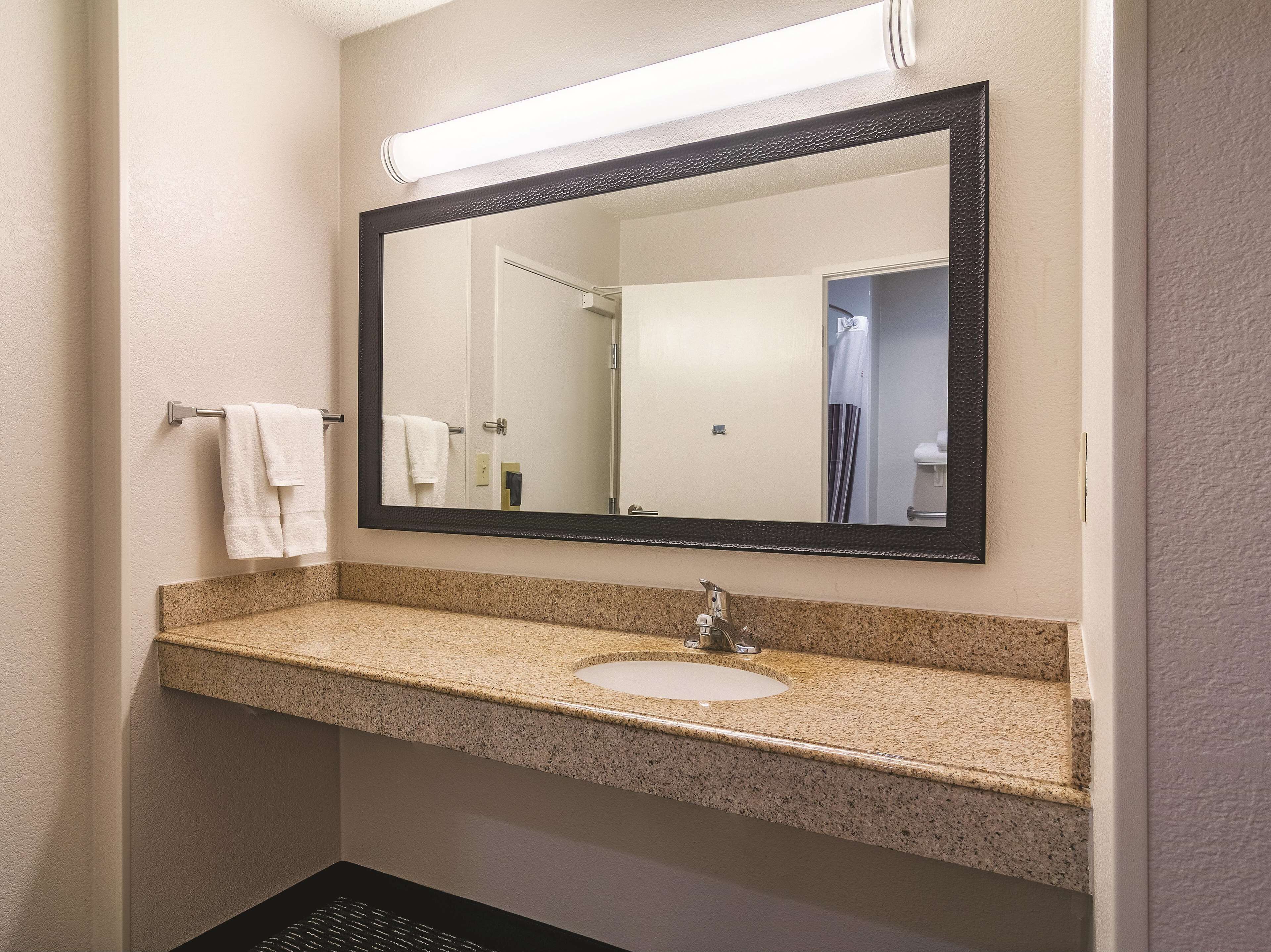A bathroom with a granite countertop sink, a large mirror, and a towel rack.