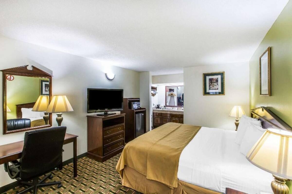 A hotel room with a bed, desk, chair, television, and a mirror.