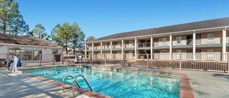A hotel with a swimming pool, a covered deck, and a multi-story building with balconies.
