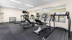 Ein Fitnessraum mit Laufbändern, Crosstrainern und einer Hantelbank.