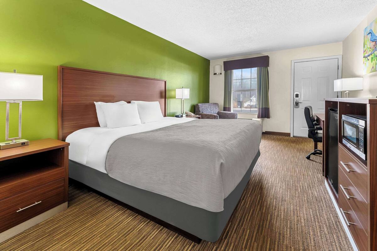 A hotel room with a large bed, a desk, a chair, a TV, and a window with curtains.