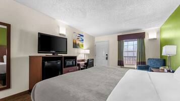 Quarto de hotel com uma cama grande, televisão de tela plana, escrivaninha com cadeira, micro-ondas e um pequeno refrigerador.