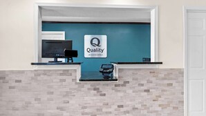 Ein Hotelrezeptionsschalter mit einem Bildschirm, einer Registrierkasse und einem Schild mit der Aufschrift 'Quality by Choice Hotels'.