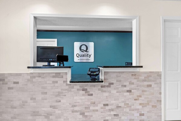 A hotel reception desk with a monitor, a cash register, and a sign that reads "Quality by Choice Hotels".