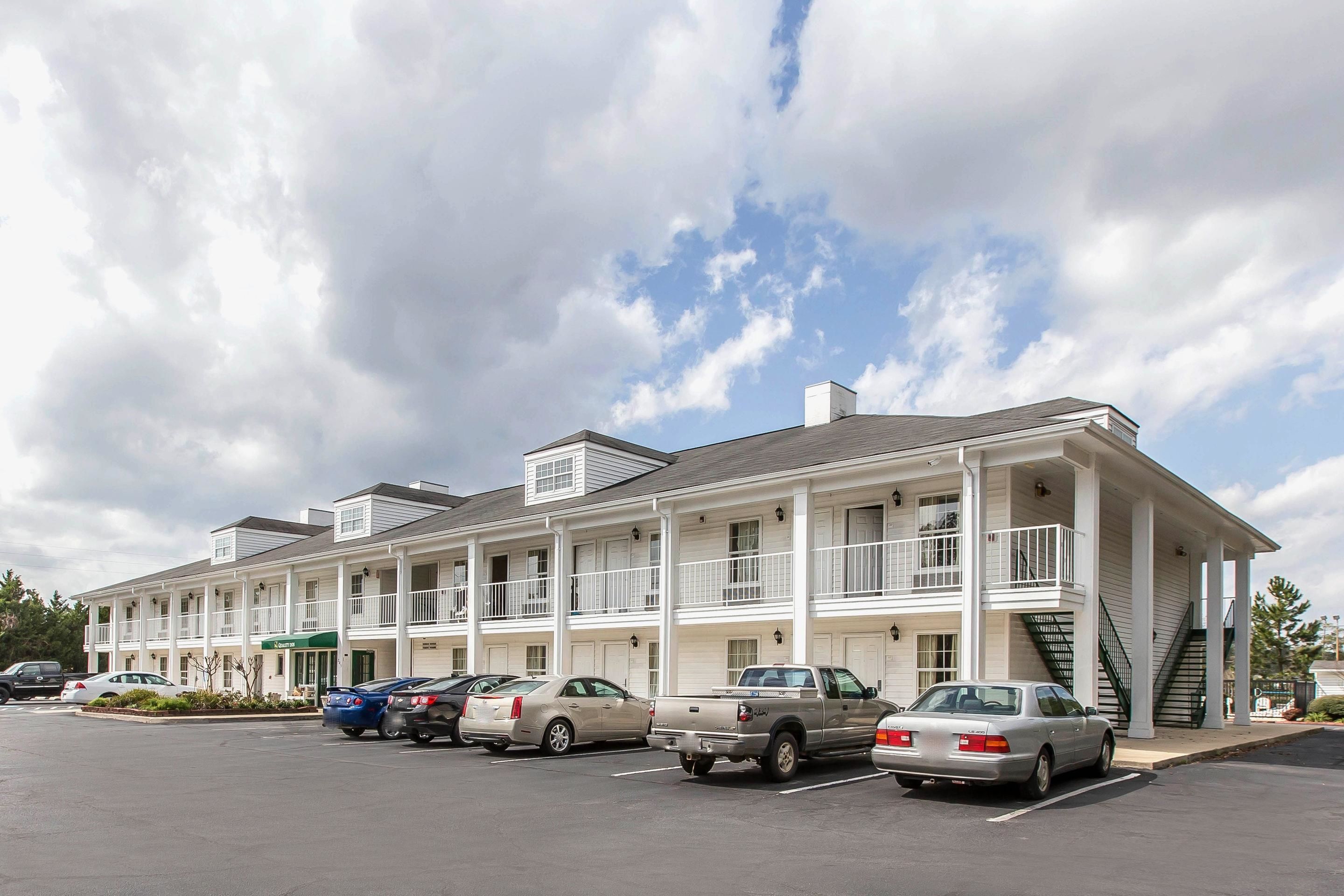 A multi-story hotel with a parking lot, featuring a row of cars parked in front.
