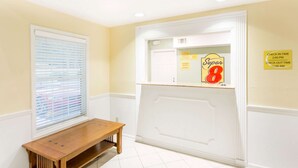 Une chambre d’hôtel avec un panneau indiquant les heures d’arrivée et de départ, un banc en bois et une fenêtre avec des stores.