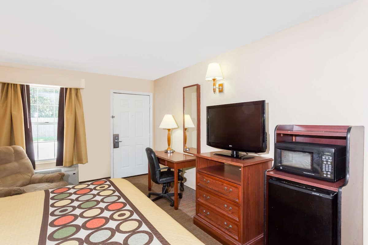 Een hotelkamer met een bed, een bureau, een televisie, een magnetron en een stoel.