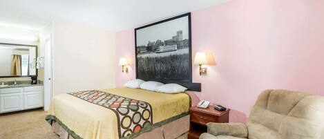 Una habitación de hotel con cama, una silla, una mesita de noche y un cuadro colgado en la pared.
