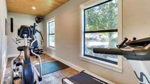 Un gimnasio con equipamiento de ejercicio, amplias ventanas y techo de madera.