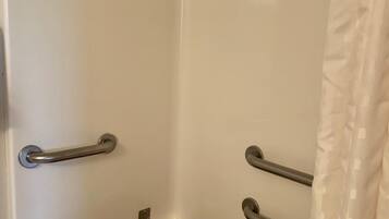 Un baño con una bañera blanca, barras de apoyo y un estante de madera.