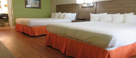 A hotel room with two beds, each with white bedding and orange skirts, a wooden headboard, and a wall-mounted lamp.