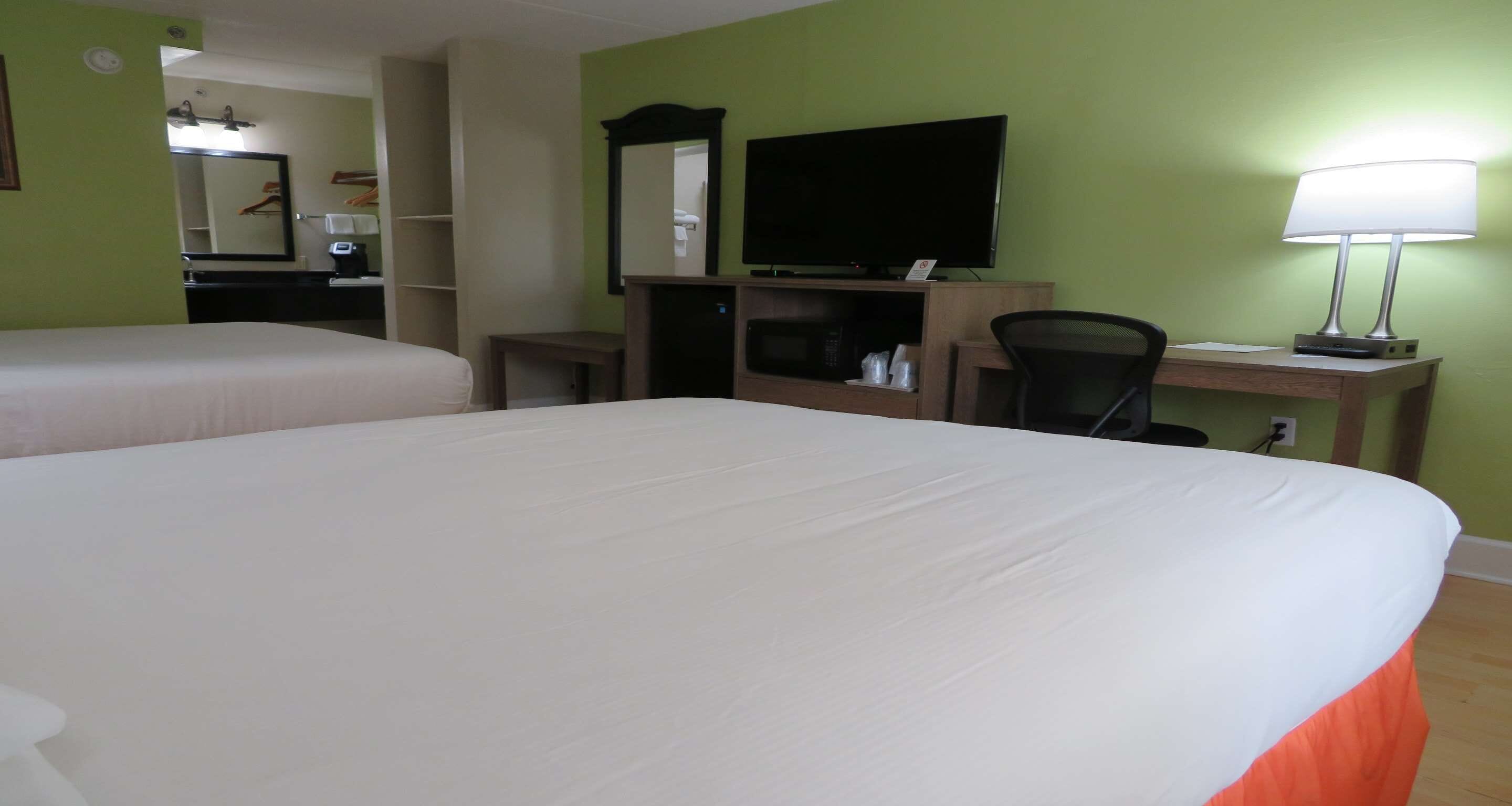 Una habitación de hotel con dos camas, un escritorio con computadora, televisor y lámpara.