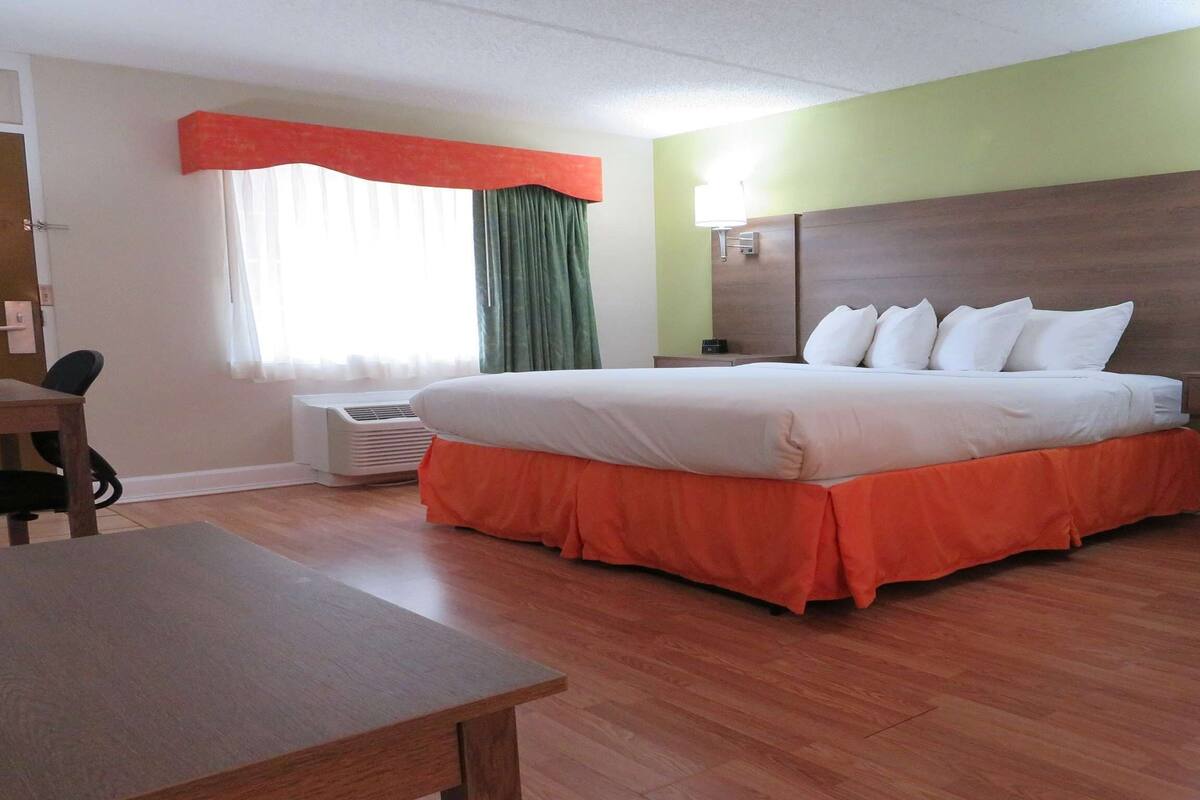 A hotel room with a large bed, a desk, a chair, a nightstand, and a wall-mounted lamp.