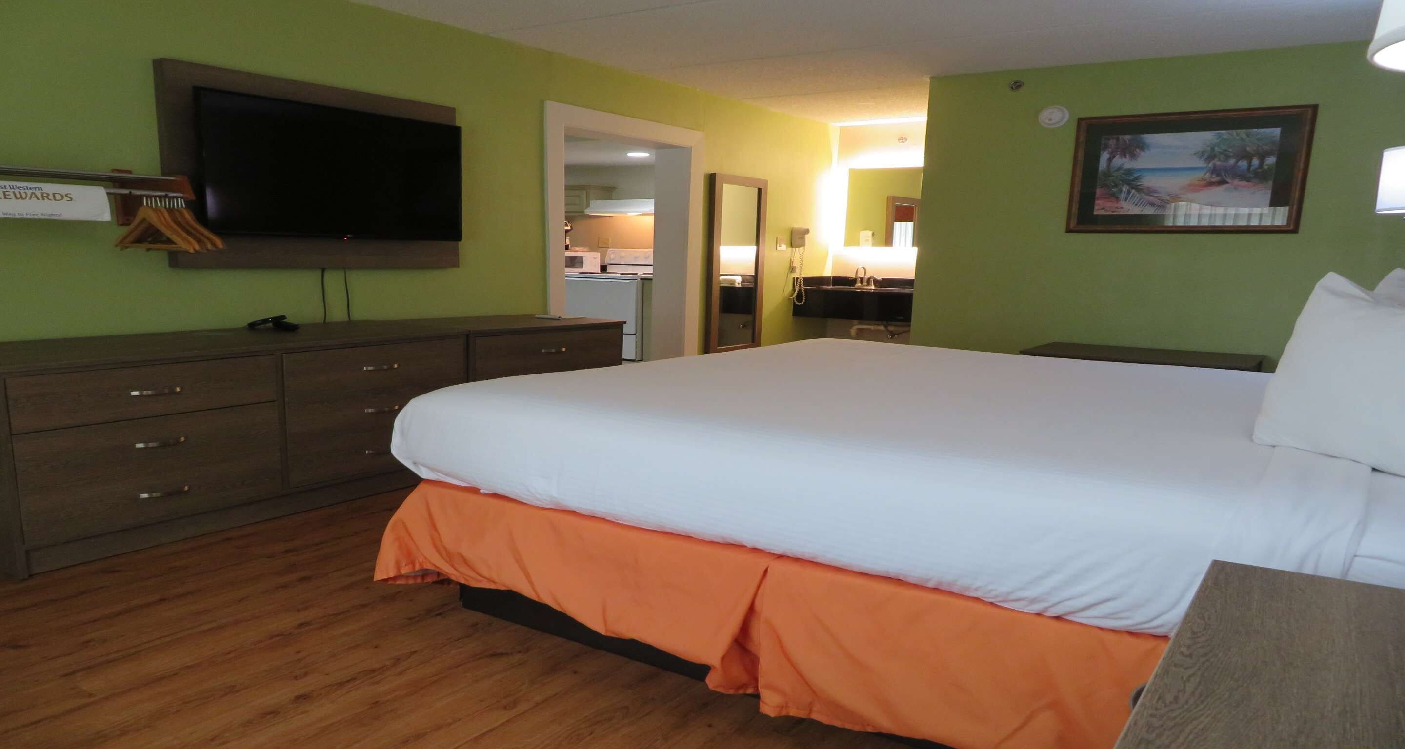Une chambre d’hôtel avec un lit, une télévision, une commode et une salle de bain visible à travers une porte ouverte.