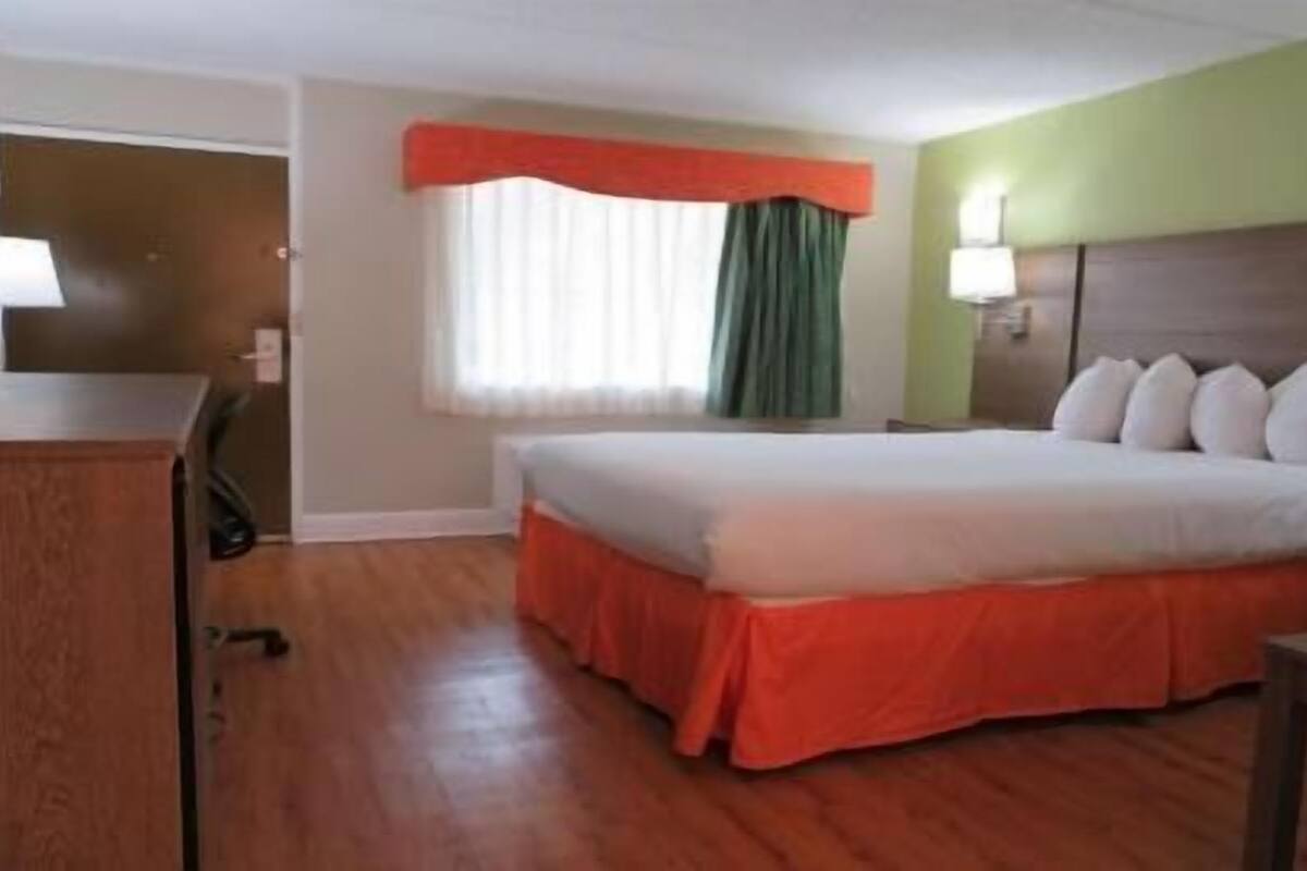 A hotel room with a bed, a desk, a window with curtains, and a lamp.