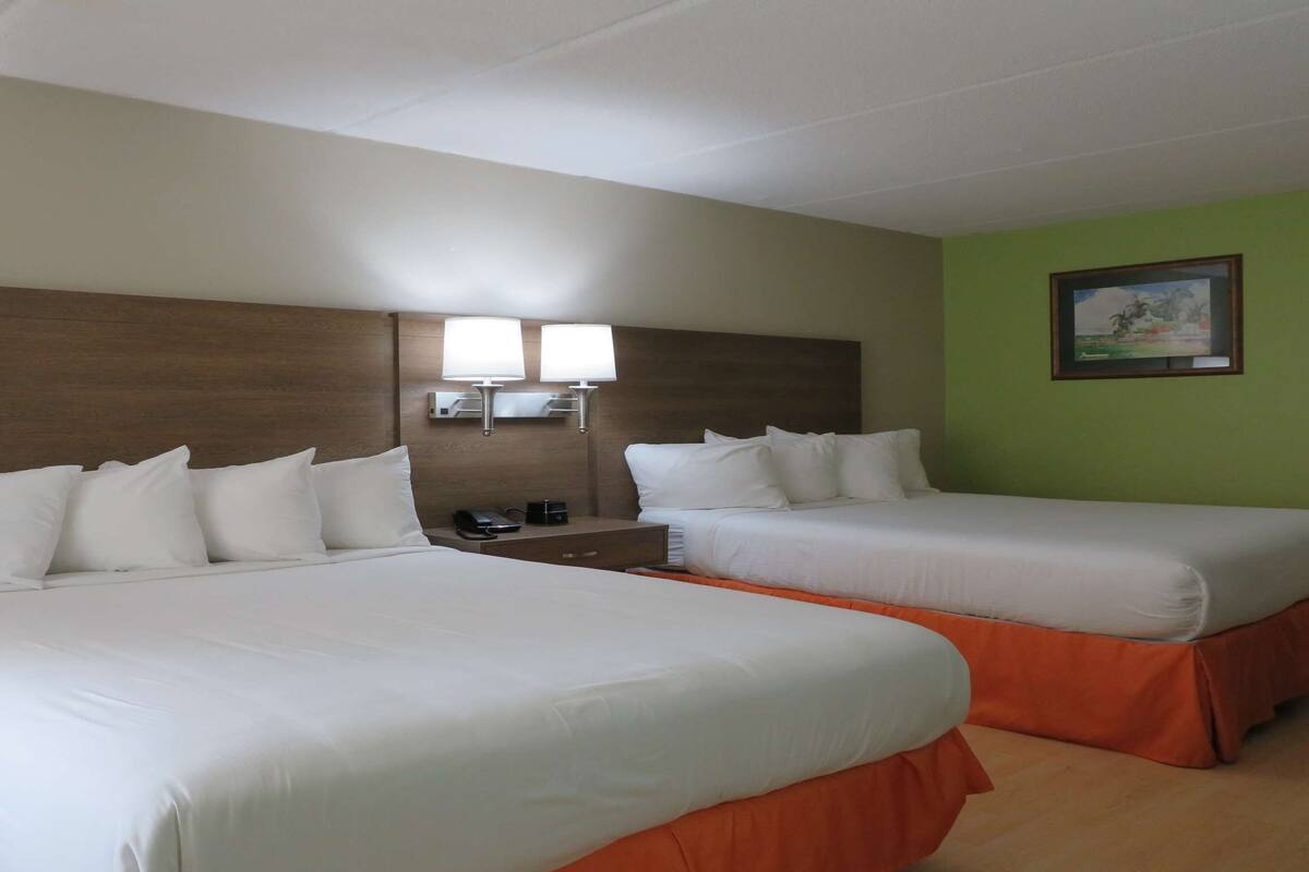 A hotel room with two beds, a nightstand, a lamp, and a painting on the wall.